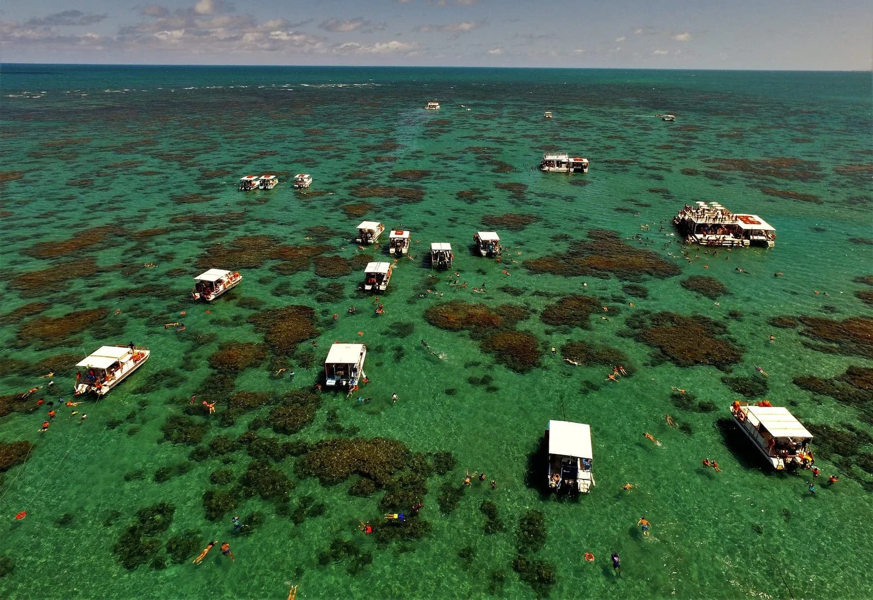 Parrachos de Maracajaú com barcos e pessoas em águas rasas sobre os recifes