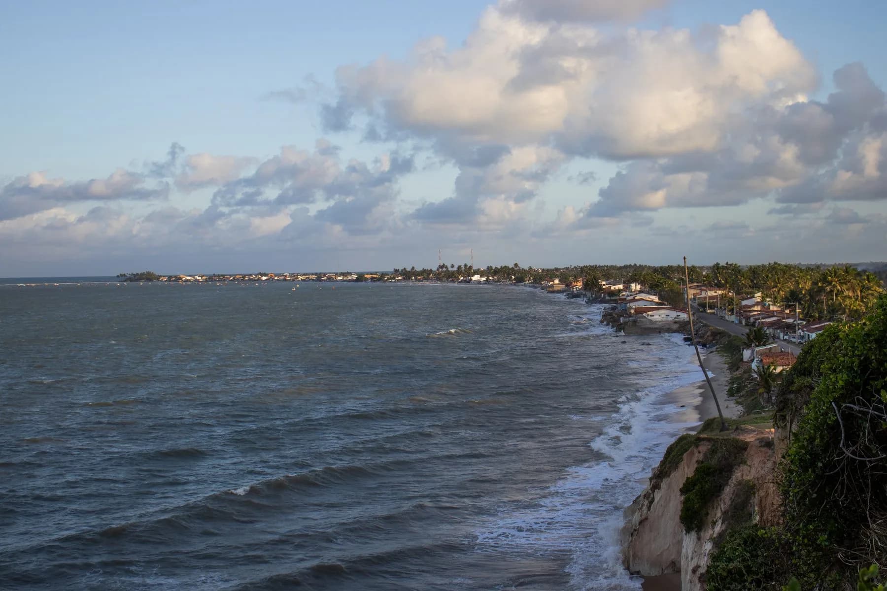 Costa de Barra de Camaratuba com casas à beira-mar e falésias sob nuvens