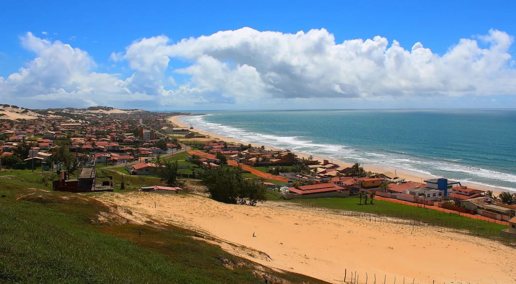 Praia de Cotovelo vista do alto, com dunas, casas e faixa de mar aberto