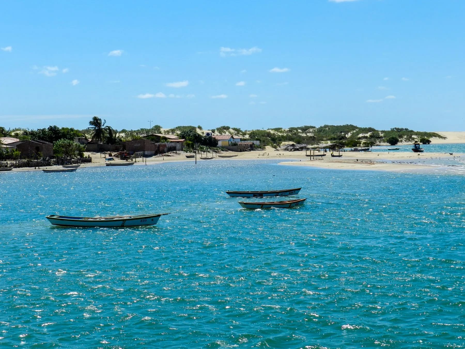 Passeio para Galinhos com barcos de pesca diante da vila à margem das águas azuis